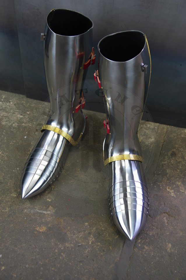 English style leg harness with fully closed cuisses, full greaves with characteristic line around outside ankles. Demi-greaves connected with greaves on rotary pin. Made of medium carbon steel of various thickness from 1 mm up to 1,5 mm. Heat hardened and tempered up to 42 HRC. Brass bands decoration motive based on example visible on Henry V tournament helm. Hand made steel buckles in set./Osony ng w stylu angielskim z w peni zamknitymi nabiodrkami, nagolennicami z charakterystyczn lini wok zewntrznej kostki. Demi-greave poczony z nagolennicami poprzez obrotowy pin. Wykonane ze stali redniowglowej rnej gruboci od 1 mm do 1,5 mm. Hartowane i odpuszczane do 42 HRC. Mosine listwy dekoracyjne z motywem wzorowanym na hemie turniejowym Henryka V. W zestawie rcznie robione sprzczki stalowe.